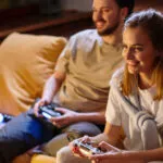 Ett par som spelar tv-spel i soffa. Tv-spel har visat sig öka social kompetens.